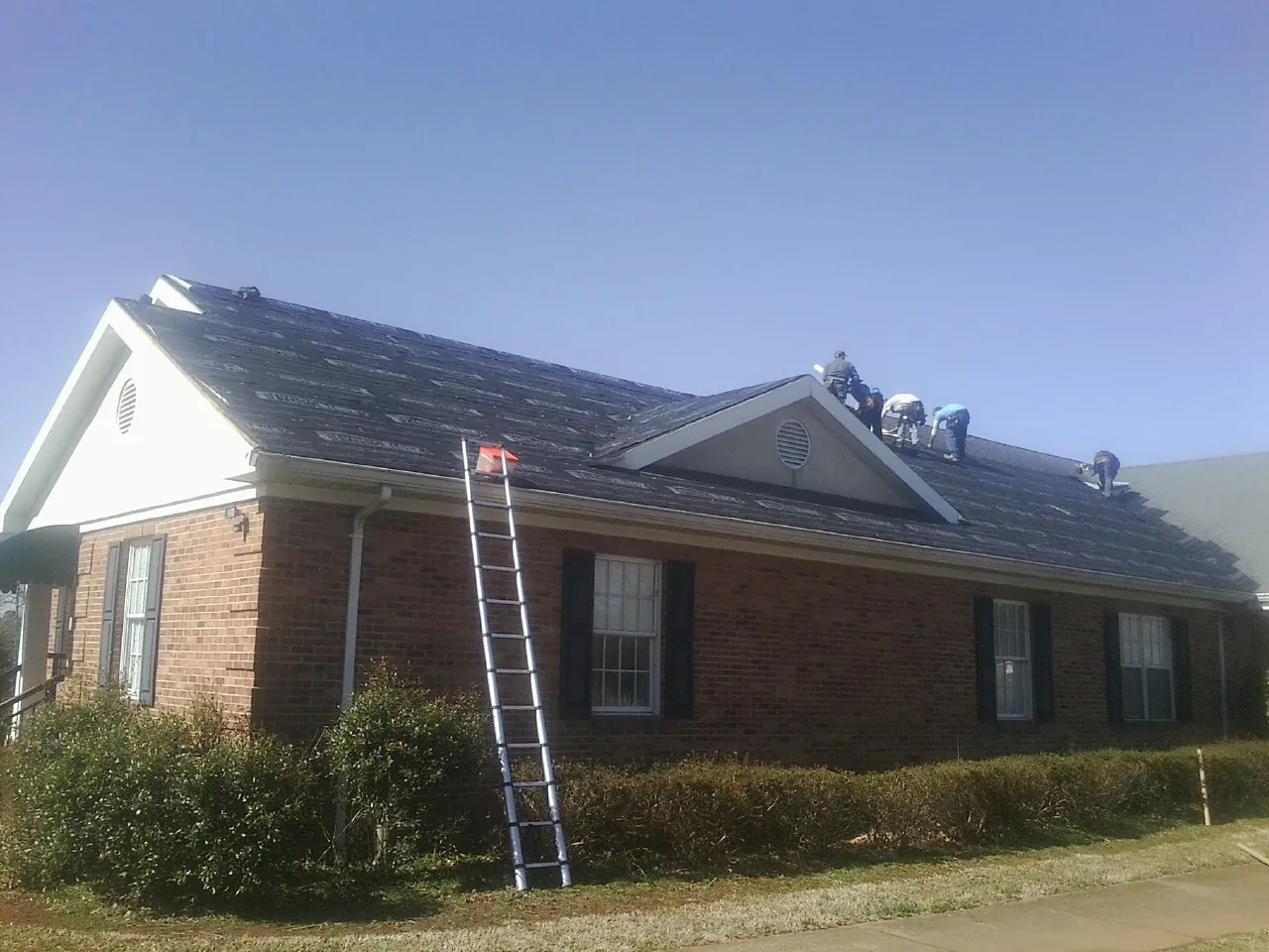 Crew tearing shingles off a brick ranch roof with a ladder set — Emergency Roof Repair work by our crew in Monroe