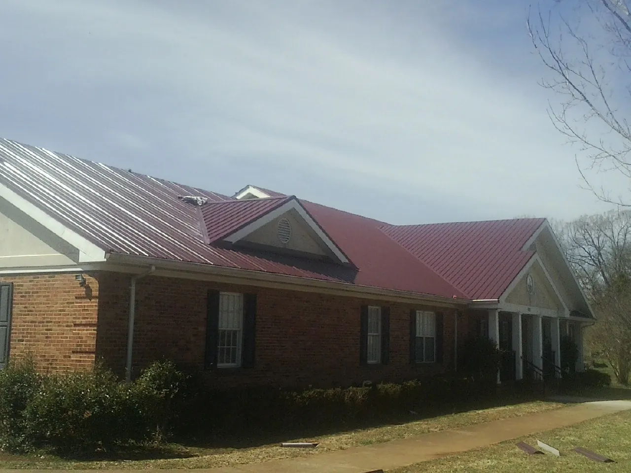 Red metal roof with gabled entries on a long brick building, from a Hail Damage Roof Repair job in Monroe