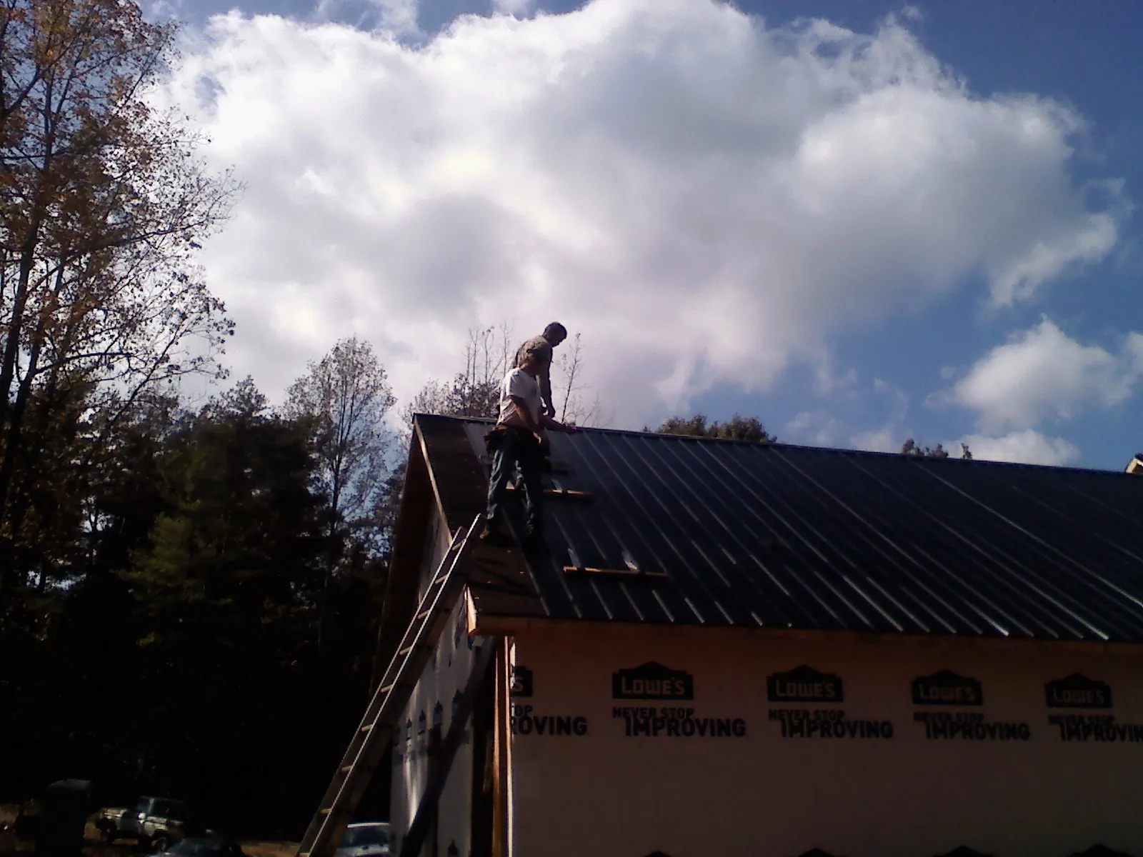 Roofer fastening dark metal panels high against a cloudy sky in Monroe
